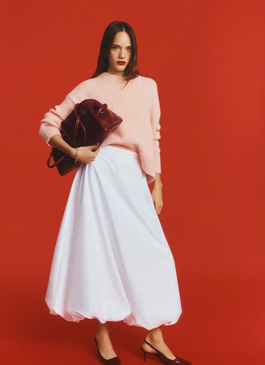 Mannequin femme portant un sac sous le bras, un pull rose et une jupe blanche